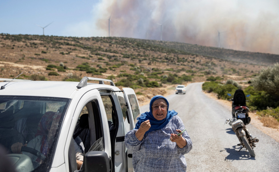 A woman reacts as smoke rises in the background during a wildfire between Urla and Cesme districts of Izmir, Turkey, July 3, 2025. REUTERS/Tuncay Dersinlioglu